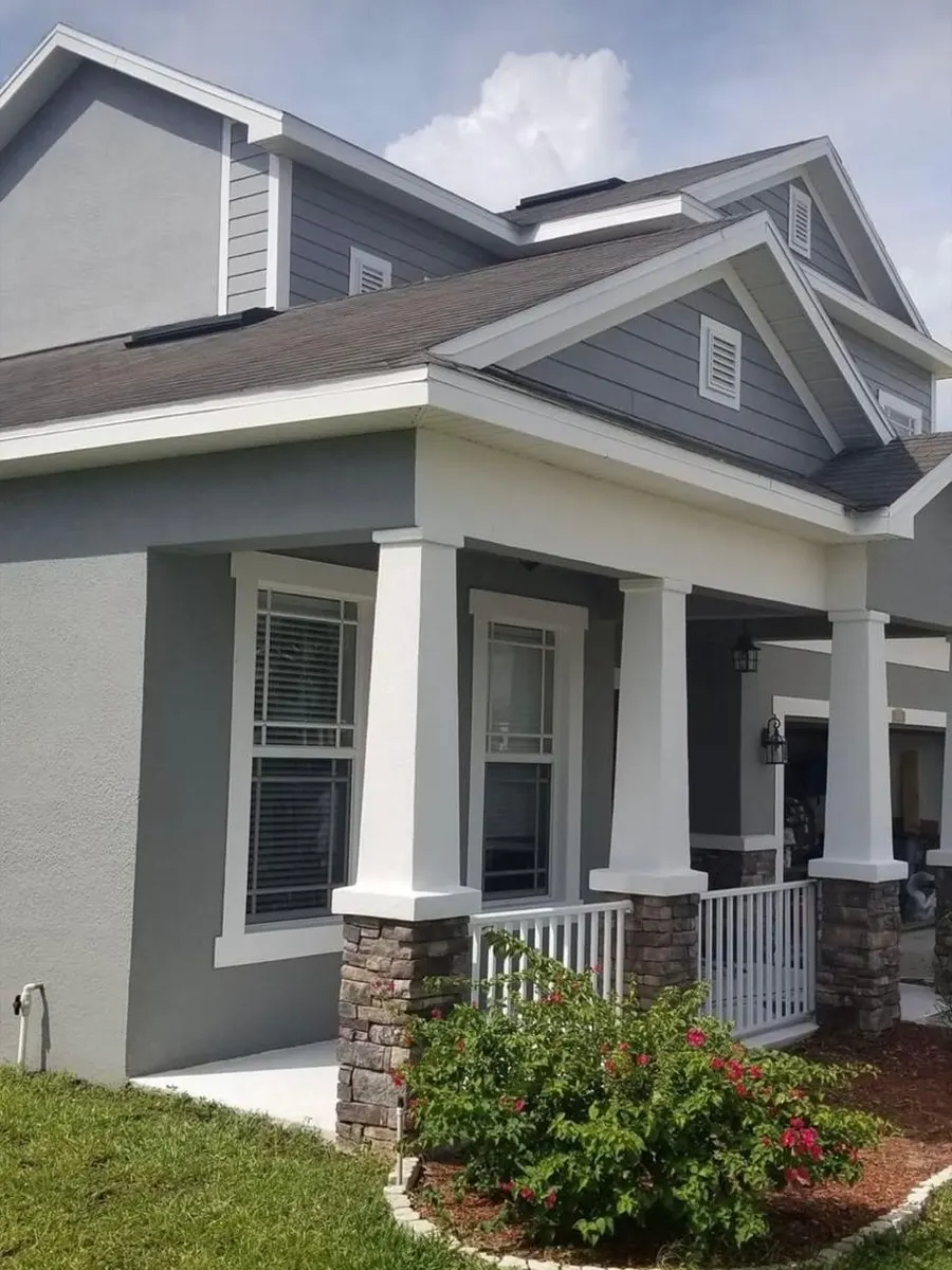 Casa de dos pisos pintada de gris con molduras blancas y columnas blancas en el porche