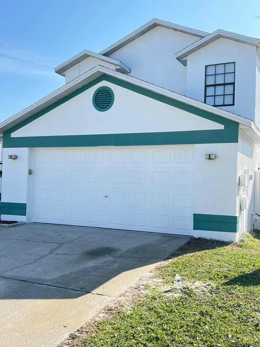 Casa de estuco de dos pisos pintada de blanco con franjas verde azulado y puerta de garaje blanca